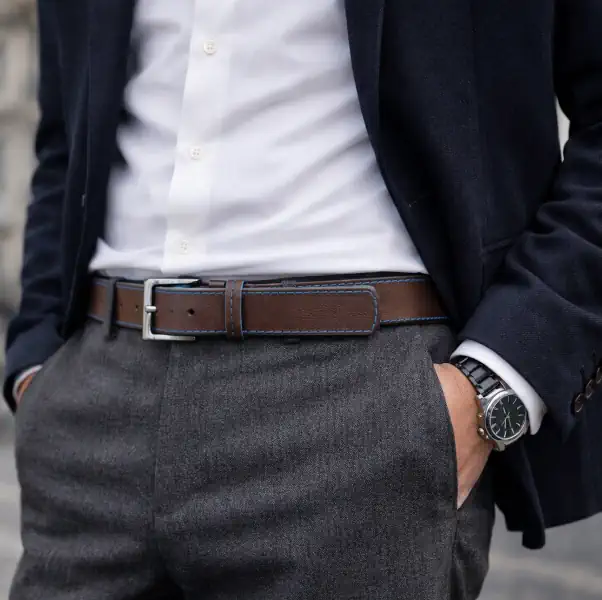 Ceinture en cuir marron avec une piqure bleu et les tranches teintées en bleu turquoise. Boucle de forme carrée, couleur canon de fusil. Ceinture portée.