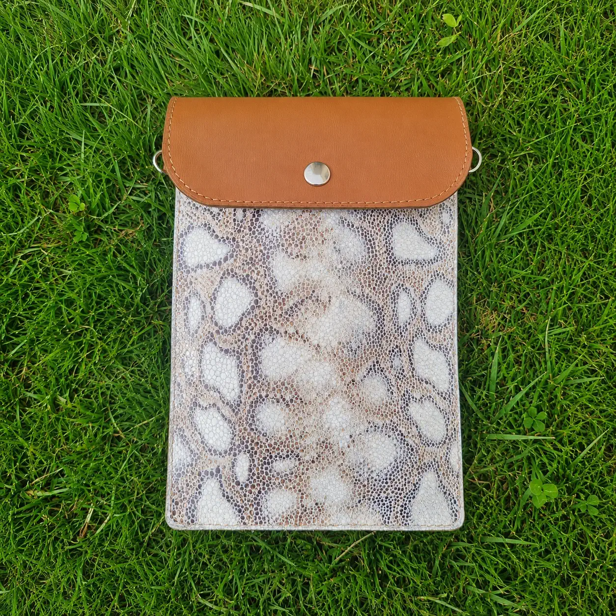 Pochette artisanale en cuir camel et beige à motifs jungle, portée en bandoulière.
