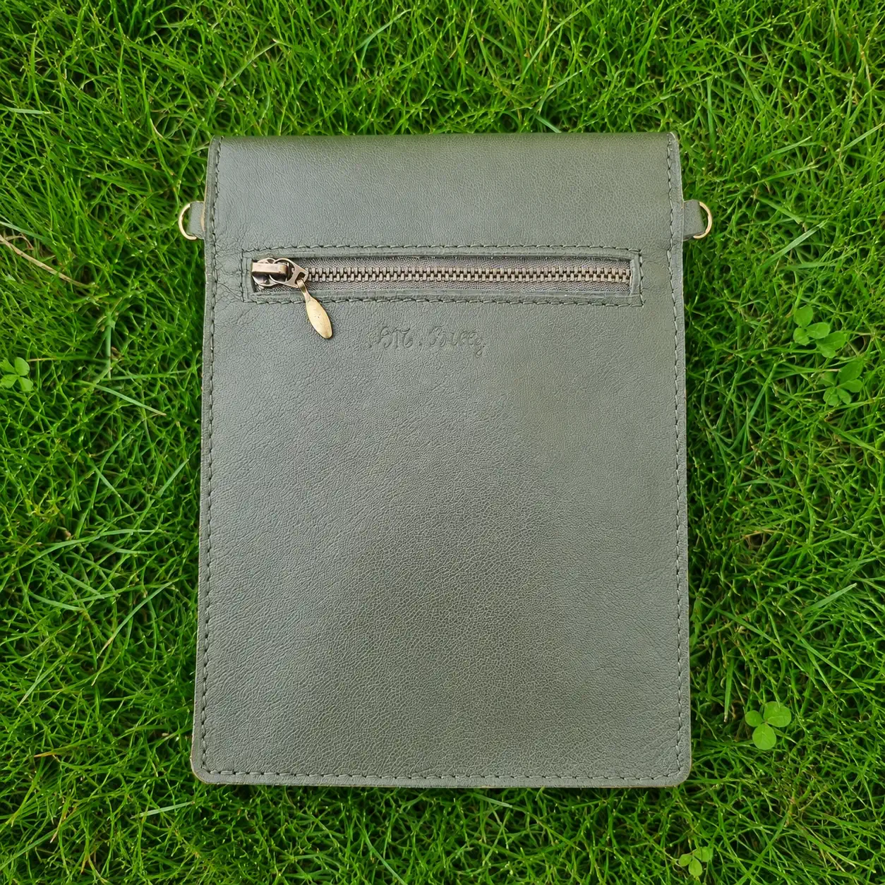 Pochette artisanale en cuir vert kaki et beige à motifs dorés, portée en bandoulière.