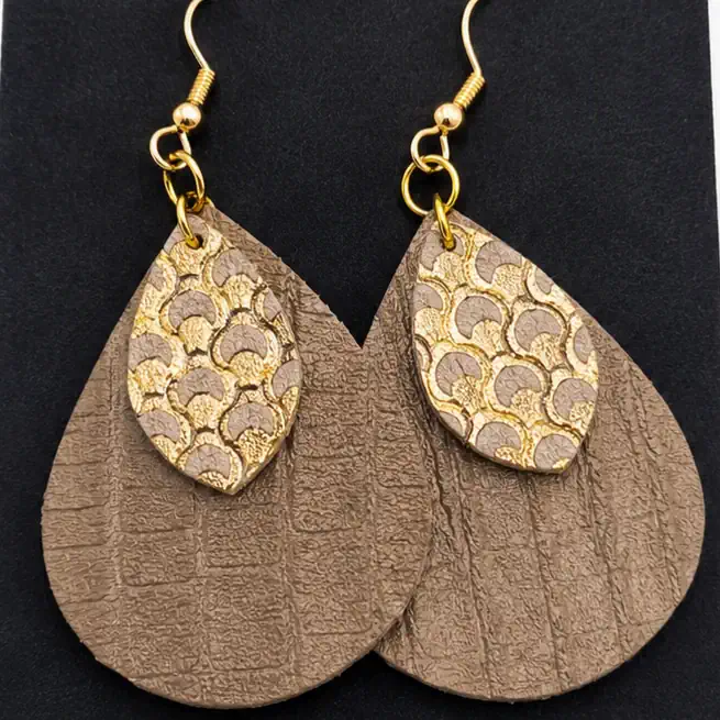 Détail de boucles d'oreilles artisanales en cuir beige taupe texturé et cuir doré
