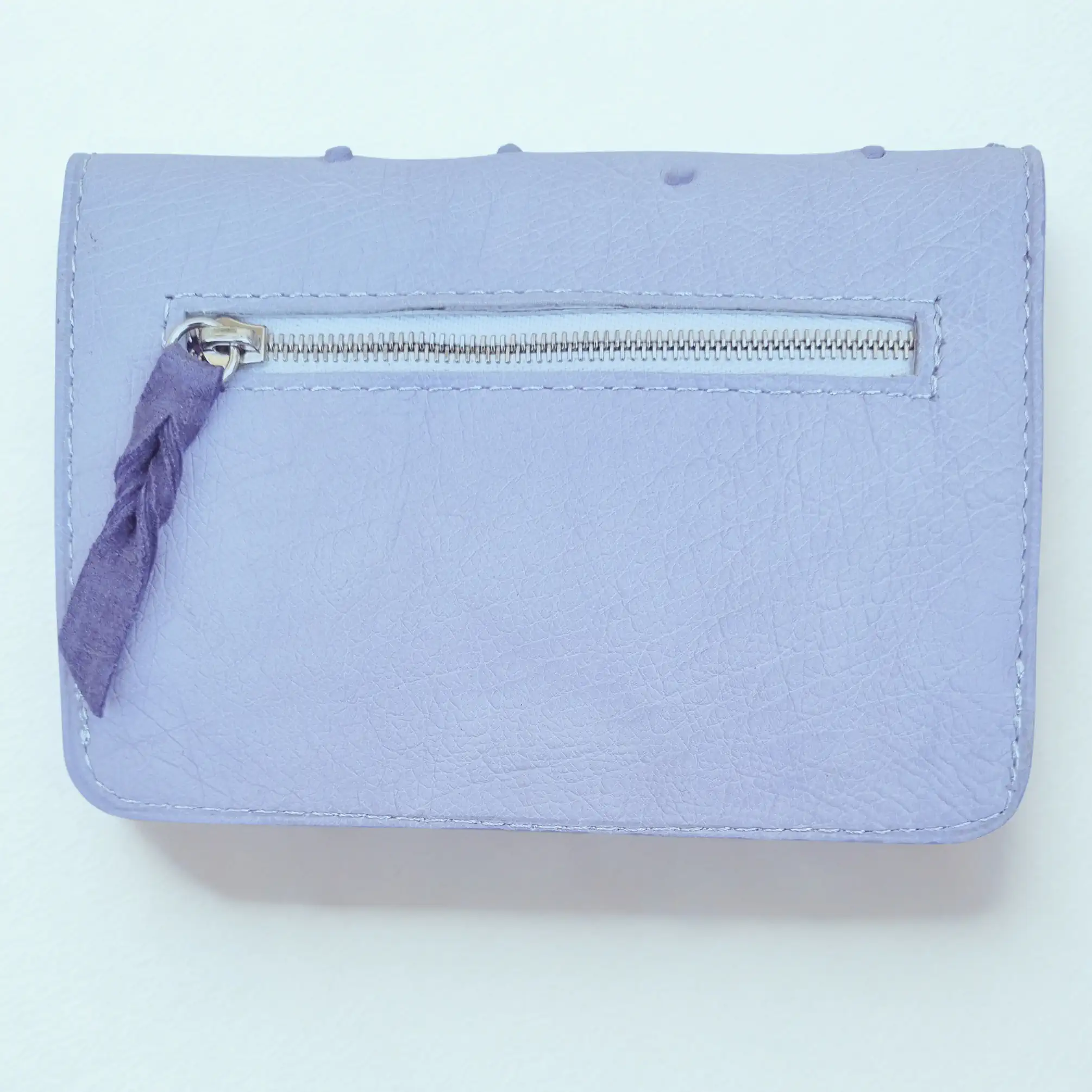 Portefeuille femme en cuir à rabats format moyen. Dos en cuir lilas avec poche zippée extérieure. Vue arrière.