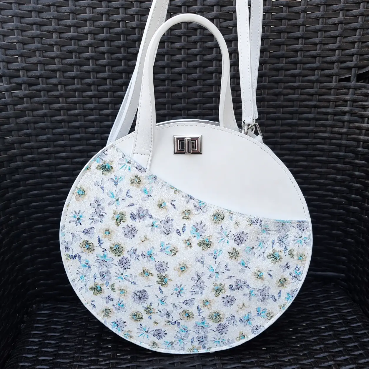 Sac rond femme en cuir blanc et imprimé fleuri pastel avec bandoulière amovible.