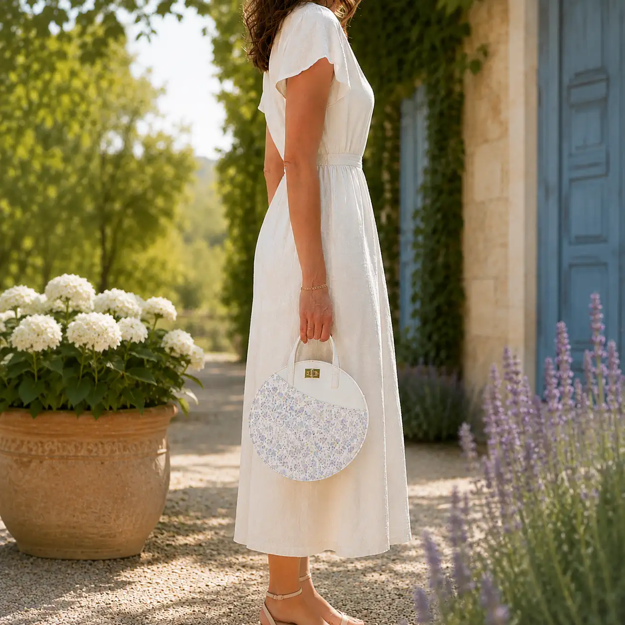 Sac rond en cuir blanc et fleuri pastel porté à la main par une femme.
